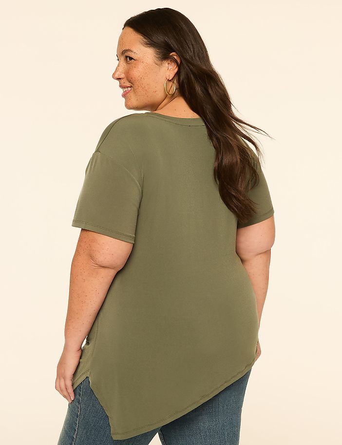 A woman in a green shirt and jeans stands against a plain, light-colored background.