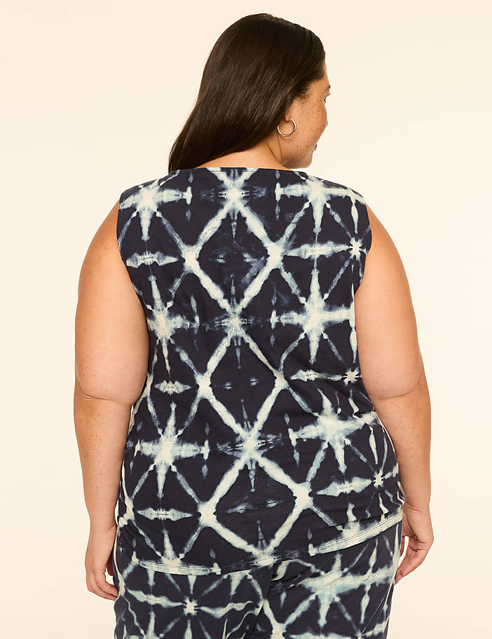 A woman with dark hair, seen from the back, wears a sleeveless tie-dye top with a diamond pattern against a plain, light-colored background.