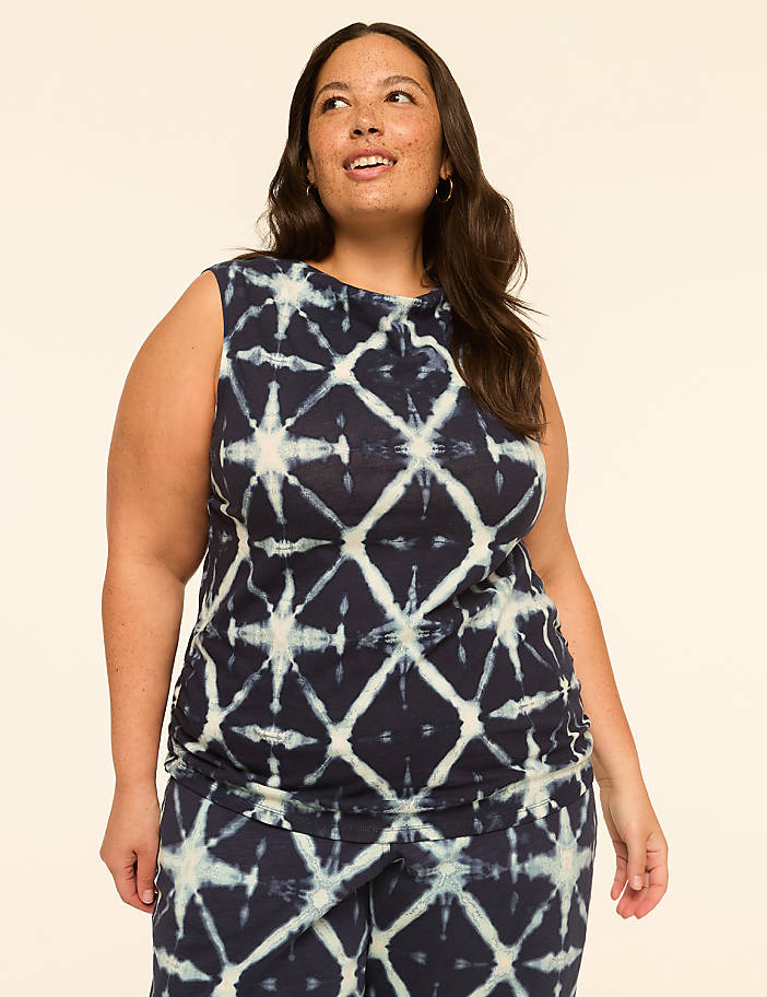 A woman with dark hair and freckles poses in a tie-dye top against a plain, light-colored background.