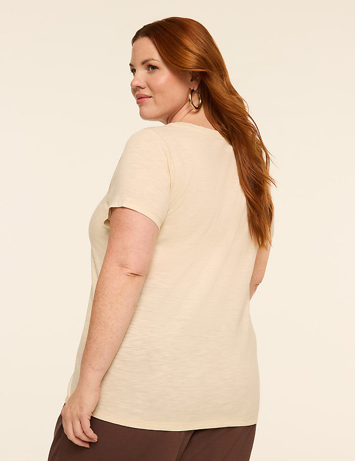 A woman with red hair and a cream-colored t-shirt stands against a plain, light background.