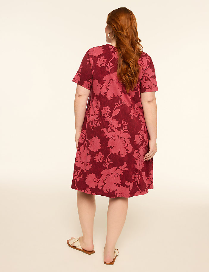 A woman with red hair wearing a floral print dress stands with her back to the camera against a plain, light-colored background.