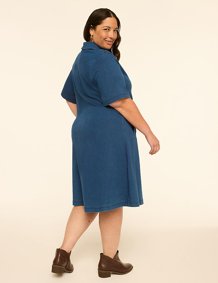 A woman in a blue dress and brown boots stands against a plain, light-colored background.