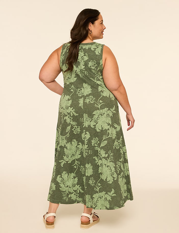 A woman in a floral green dress stands against a plain, light-colored background.