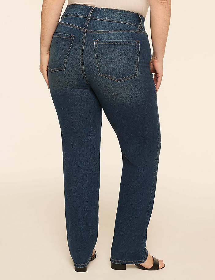 A person wearing dark wash denim jeans stands against a plain, light-colored background.