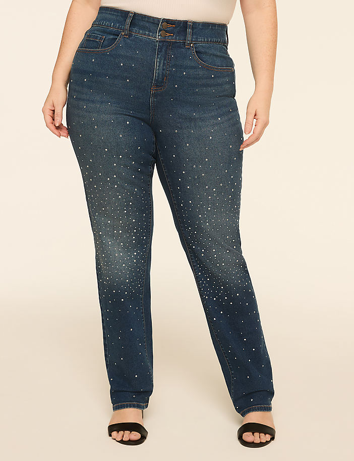 A person stands in the foreground wearing embellished denim jeans and black sandals, against a plain, light-colored background.