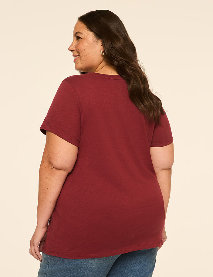 A woman in a maroon t-shirt and blue jeans stands against a plain, light-colored background.