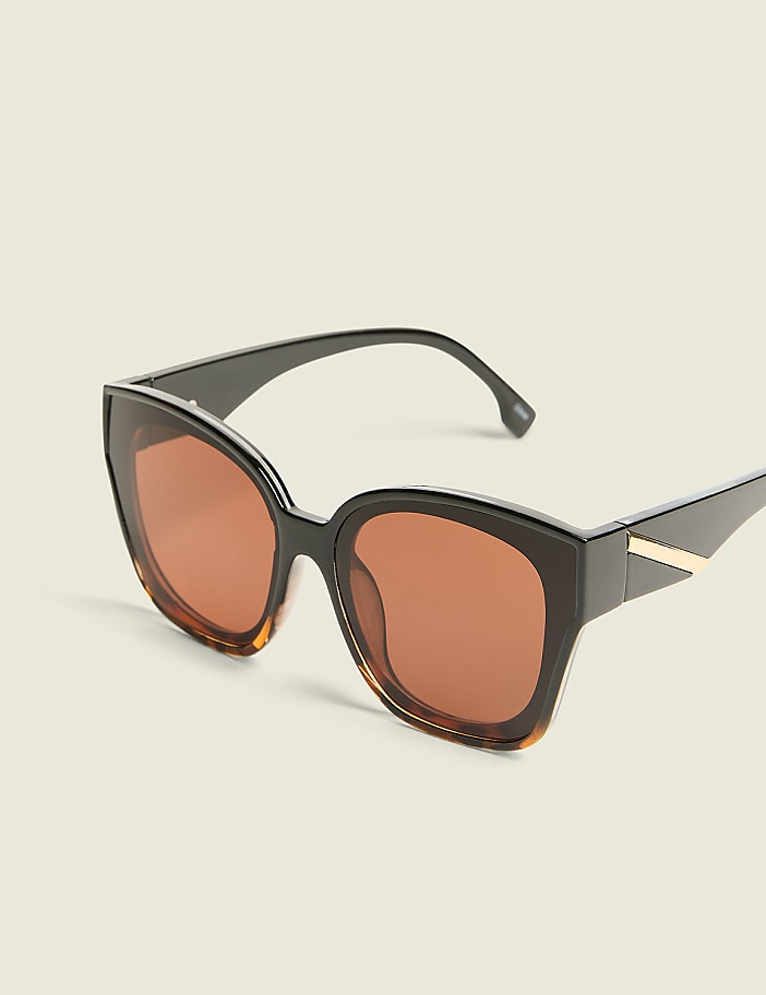 A pair of oversized, dark-rimmed sunglasses with amber lenses rests against a plain, light-colored background.