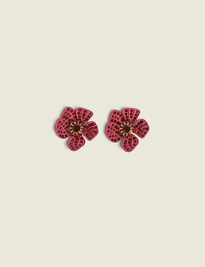 Two pink floral earrings with red gem centers rest on a pale yellow background.