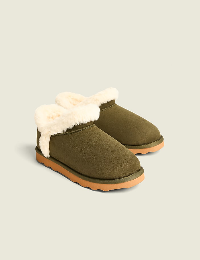 A pair of fuzzy green ankle boots with tan soles rests on a plain, light-colored background.
