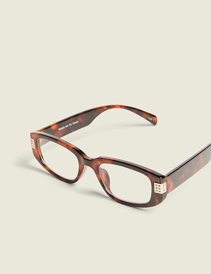 Tortoiseshell glasses with jeweled accents rest on a plain, light-colored surface.