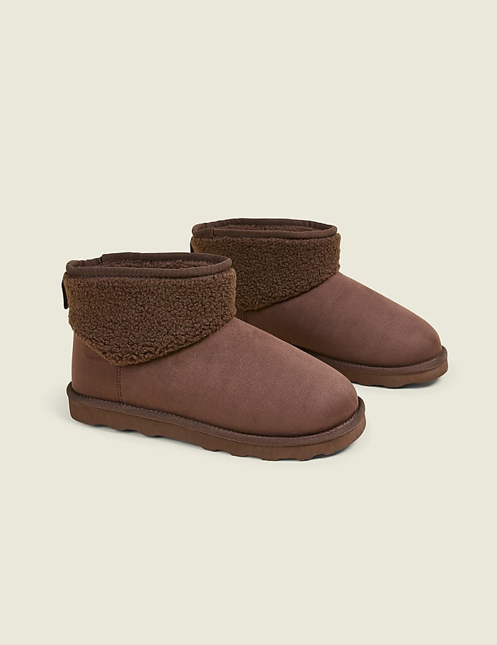 A pair of brown, fuzzy-lined ankle boots rests on a plain, light brown background.
