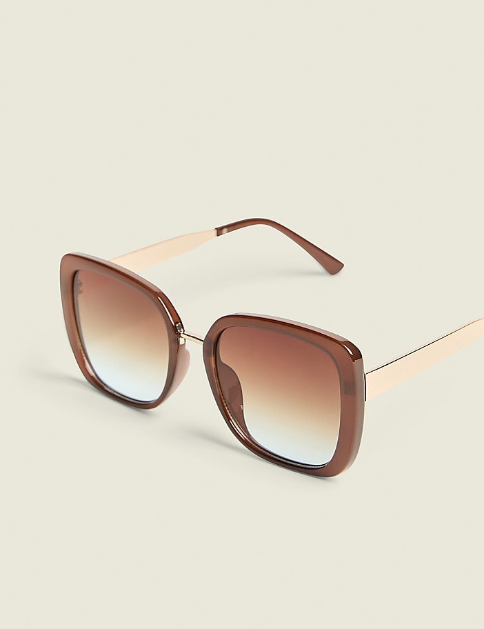 Oversized square brown sunglasses with gradient lenses rest on a plain, light-colored surface.