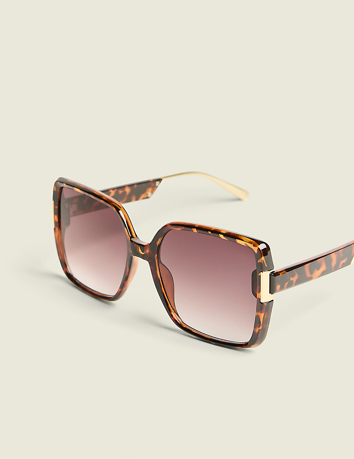 Oversized tortoiseshell sunglasses with gradient lenses rest on a plain, light-colored background.