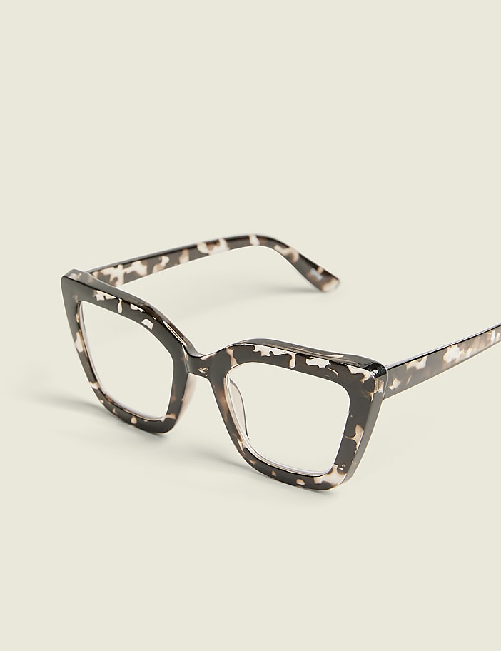 A pair of tortoiseshell cat-eye glasses rests on a plain, light-colored surface.