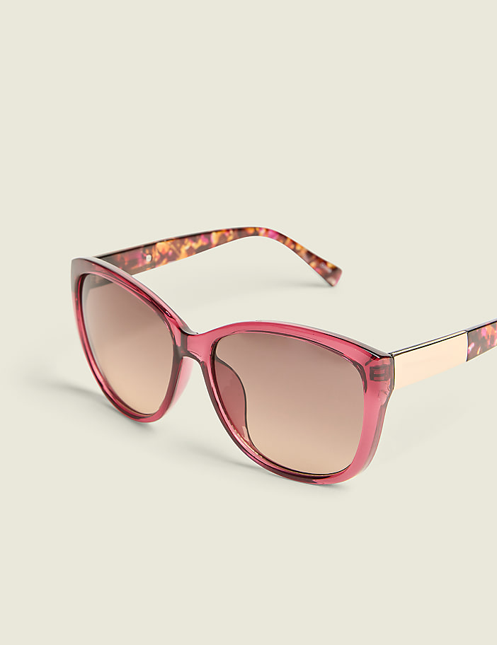 A pair of pink cat-eye sunglasses with brown lenses rests on a plain white background.