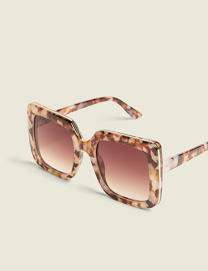 Oversized tortoiseshell sunglasses with gradient brown lenses rest on a plain, light-colored surface.