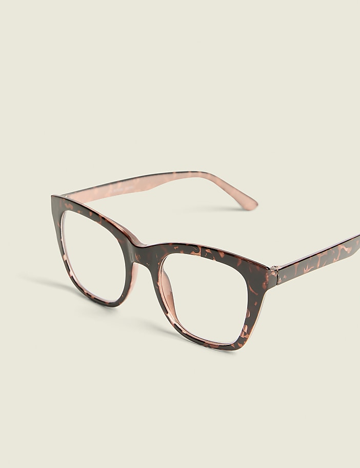 A pair of tortoiseshell cat-eye glasses with rose gold temples rests on a plain, light-colored background.