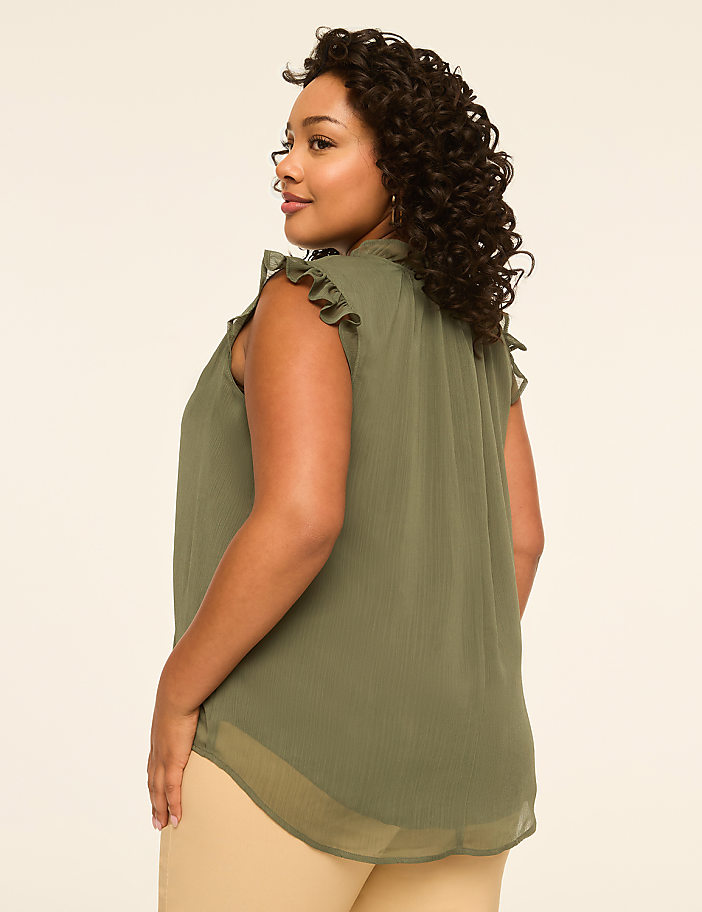 A woman in a green ruffled top stands against a plain, light-colored background.