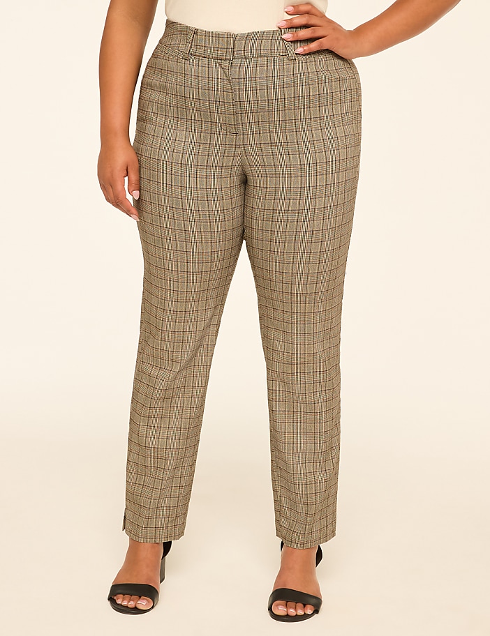 A woman in plaid pants and black heels stands against a plain, light-colored background.