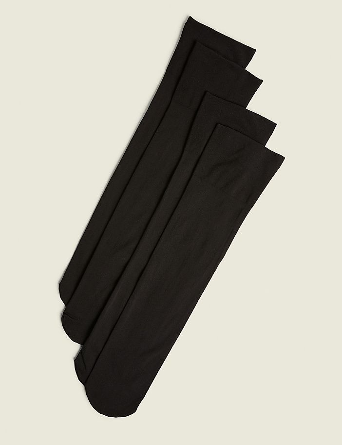 Four black knee-high socks are neatly arranged diagonally on a plain, light beige background.