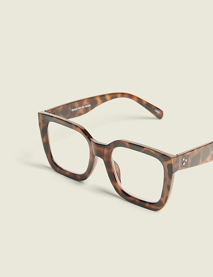 Tortoiseshell square-framed glasses with clear lenses rest on a plain, light-colored background.