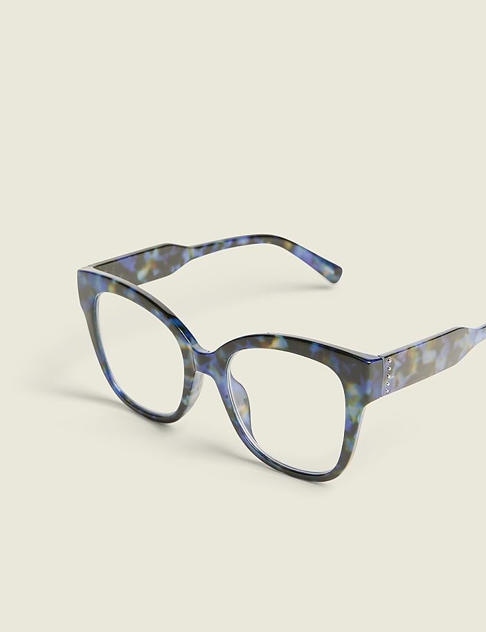 A pair of blue tortoiseshell glasses rests on a plain, light-colored surface against a soft, off-white background.