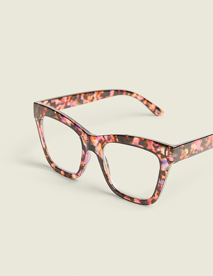 A pair of cat-eye glasses with a tortoiseshell pattern rests on a plain, light-colored surface.
