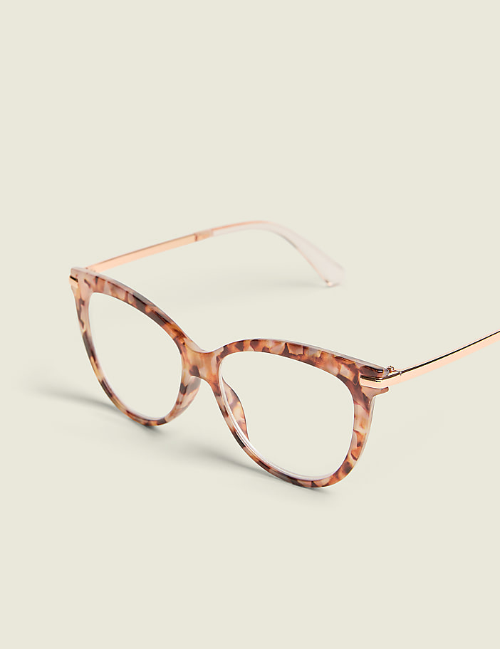 A pair of cat-eye glasses with a tortoiseshell pattern and rose gold temples rests on a plain, light-colored surface.