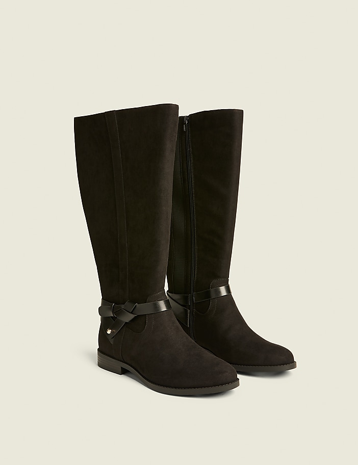 A pair of black suede knee-high boots with buckle accents are displayed against a plain, light-colored background.