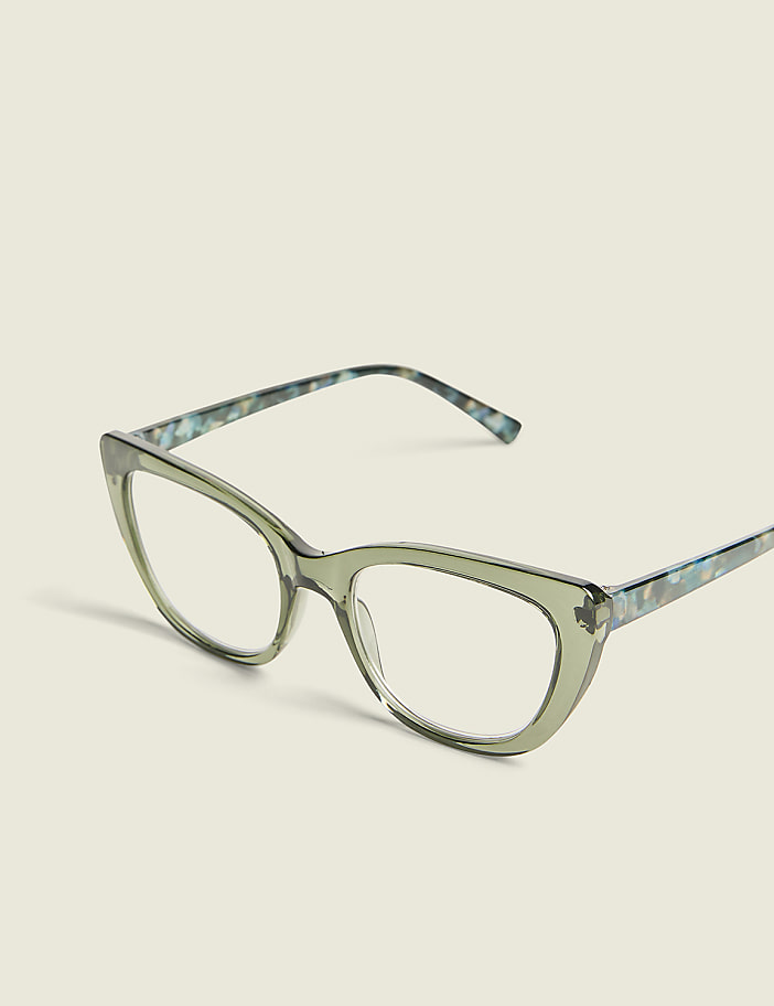 A pair of light green cat-eye glasses with a speckled pattern on the temples rests on a plain, light-colored background.