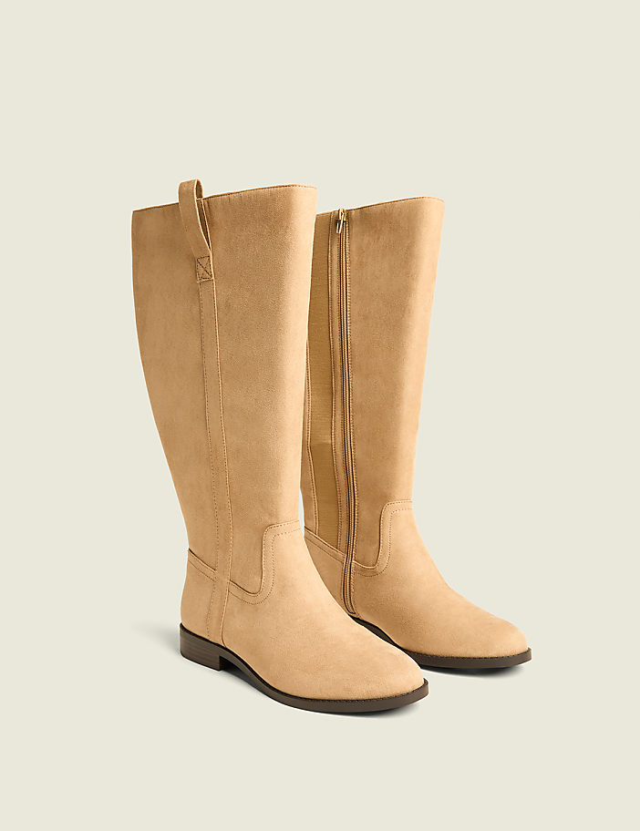 A pair of tan suede knee-high boots with a side zipper stand on a plain, light-colored background.