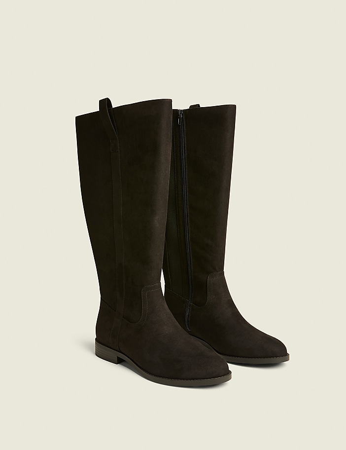 A pair of dark brown, knee-high suede boots with zippers are displayed against a plain, light beige background.