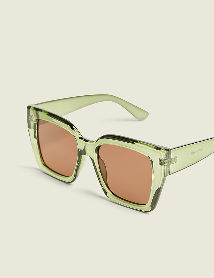 A pair of light green, oversized sunglasses with brown lenses rests on a plain, light-colored background.