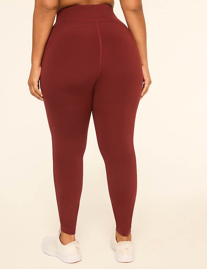 A person wearing maroon leggings and white sneakers stands against a plain, light-colored background.
