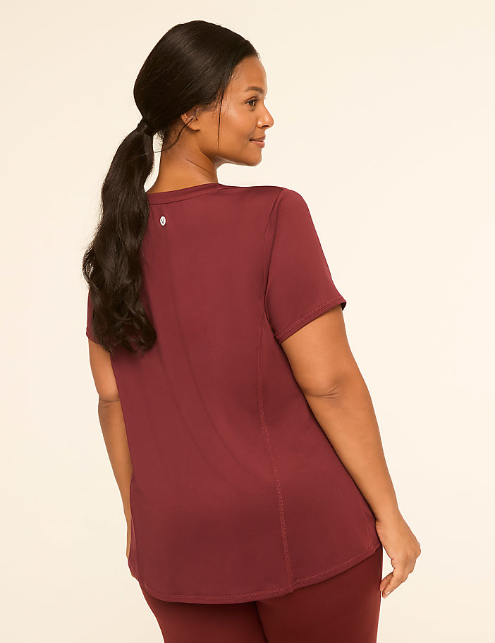 A woman in a maroon t-shirt and leggings stands against a plain, light-colored background.