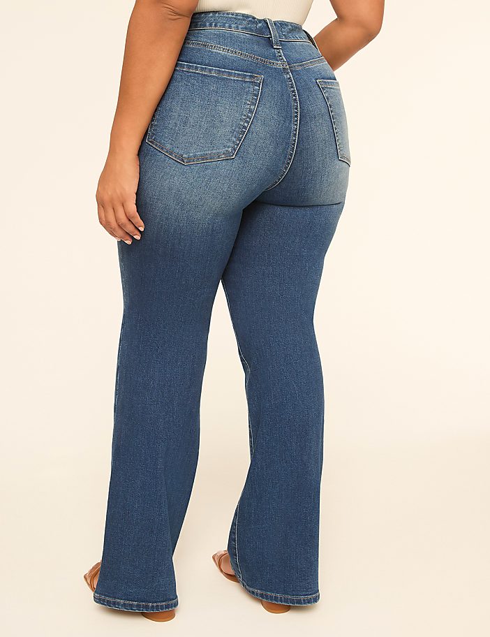 A person wearing flared blue jeans stands against a plain, light-colored background.