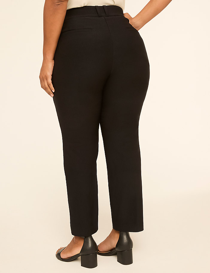 A person wearing black pants and black heels stands against a plain, light-colored background.