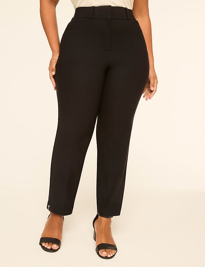 A person in black pants and heels stands against a plain, light-colored background.