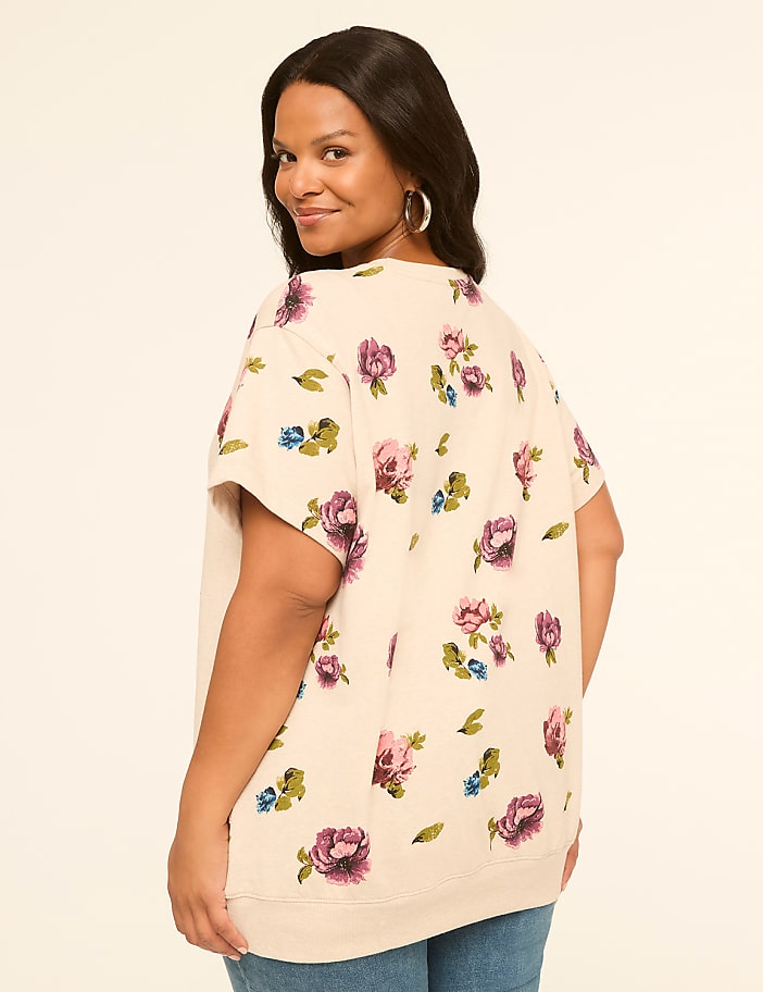 A woman in a floral print top and jeans smiles over her shoulder against a plain, light background.