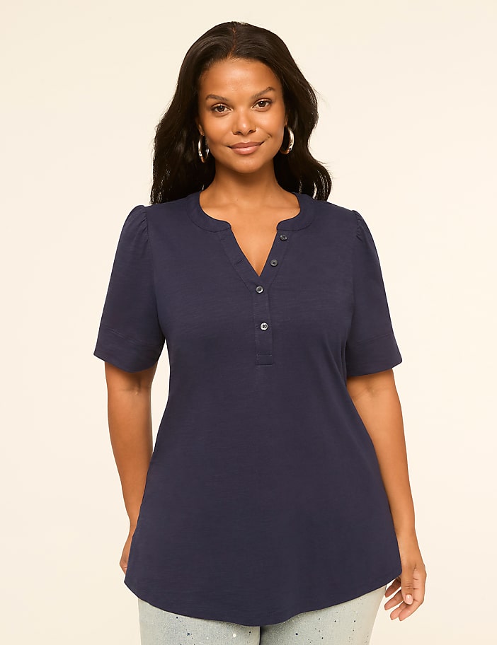 A woman in a navy blue henley shirt stands against a plain, light-colored background.