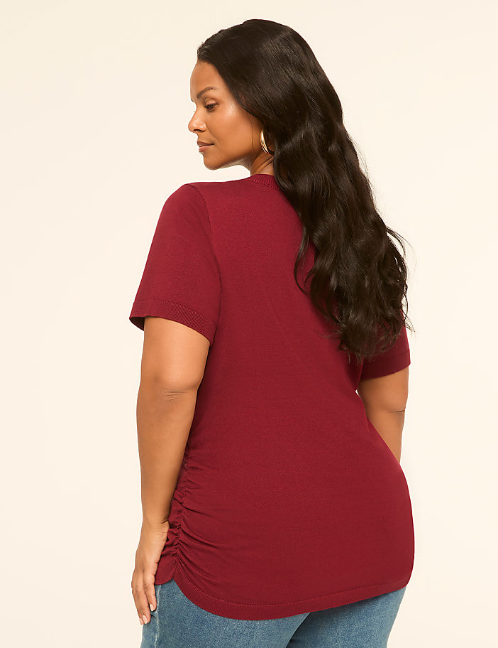 A woman in a maroon t-shirt and jeans stands against a plain, light-colored background.