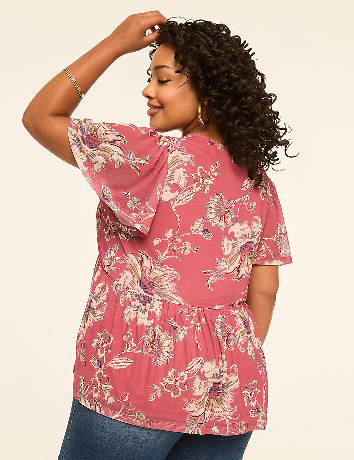 A woman in a floral print top and jeans poses against a plain background.