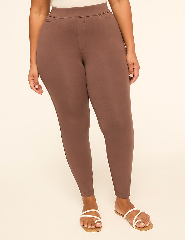 A person wearing brown leggings and white sandals stands against a plain, light-colored background.