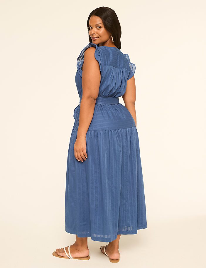 A woman in a blue dress stands against a plain, light-colored background.