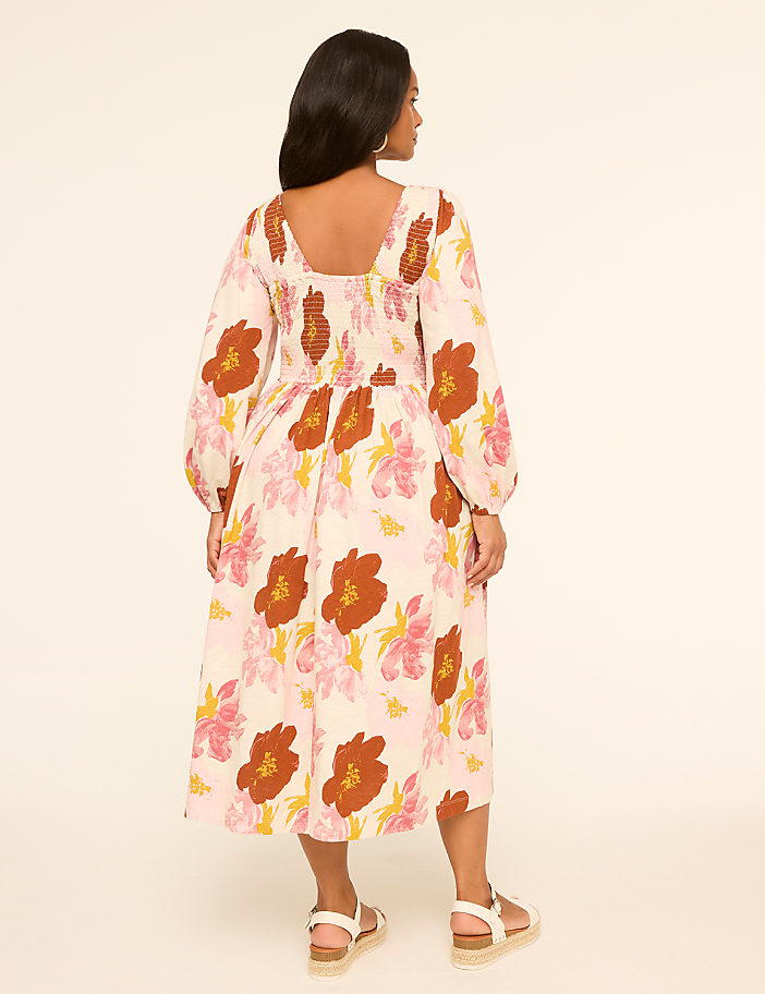 A woman in a floral print dress stands against a plain, light-colored background.