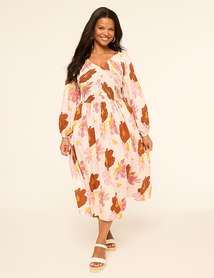 A woman in a floral dress stands against a plain, light-colored background.
