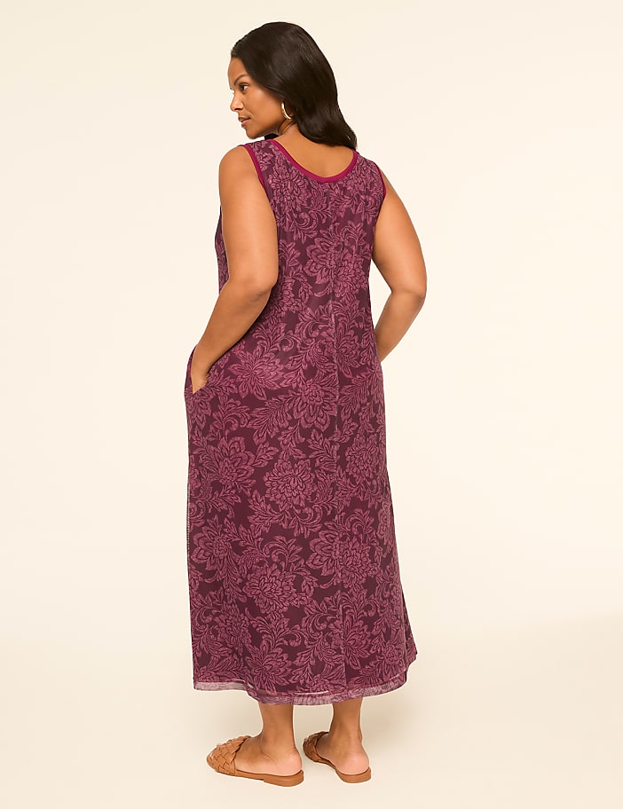 A woman in a floral print dress stands with her hands in her pockets against a plain, light background.