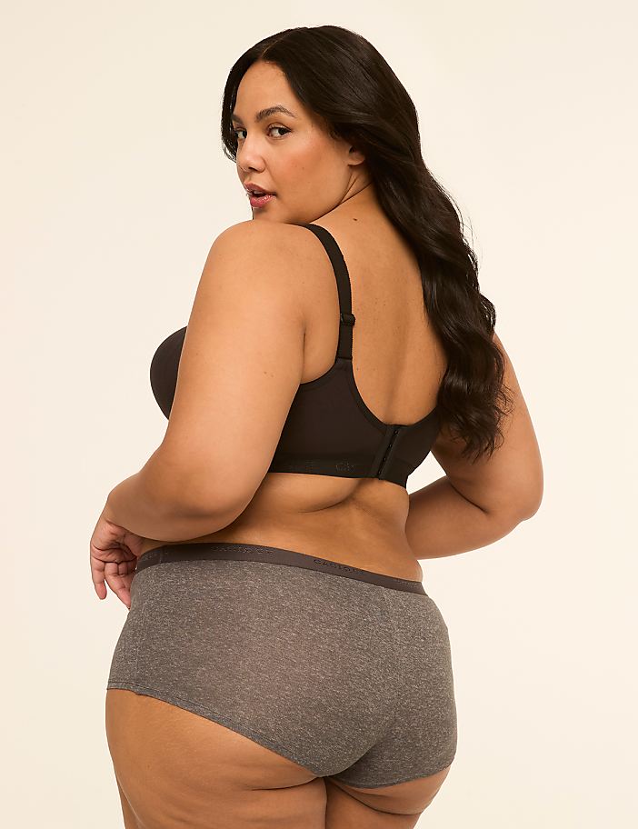 A woman in a black bra and grey underwear poses against a plain, light-colored background.