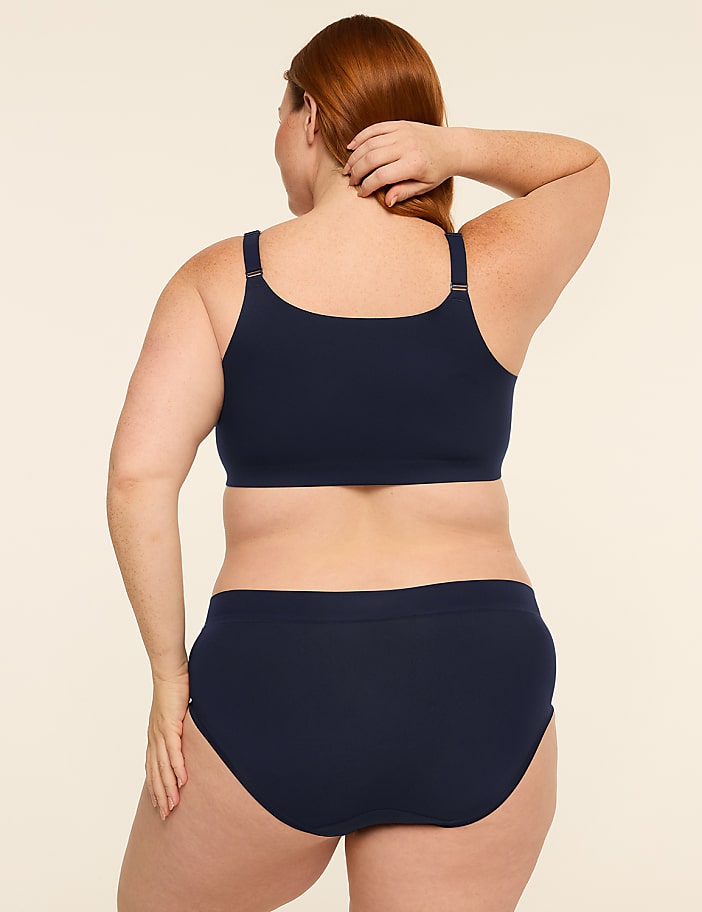 A woman with red hair, seen from behind, wears a navy blue bra and underwear against a plain, light-colored background.