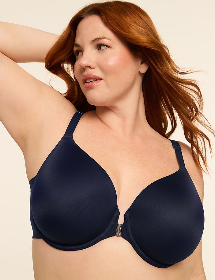 A woman with auburn hair poses in a navy blue bra against a plain, light-colored background.